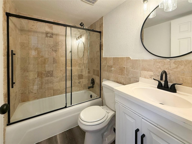 1799 N Highland Ave Unit 143, Clearwater, FL 33755 - bathroom featuring tile walls, shower / bath combination with glass door, toilet, vanity, and a textured ceiling