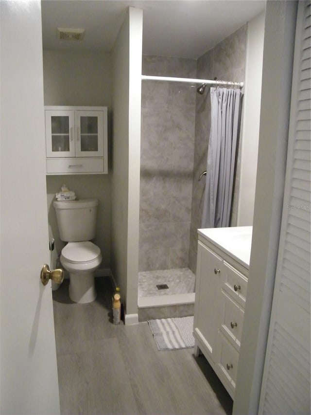 full bath featuring a tile shower, visible vents, toilet, wood finished floors, and vanity