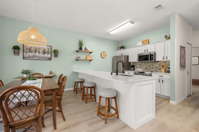 4722 Flagler Beach Way, Kissimmee, FL 34746 - kitchen with a breakfast bar area, decorative backsplash, light wood-style flooring, visible vents, and stainless steel appliances