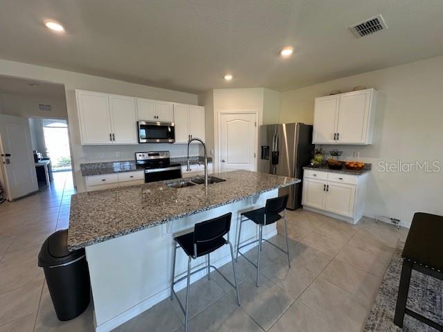 4373 Deleon St, Haines City, FL 33844 - kitchen with appliances with stainless steel finishes, a breakfast bar, a sink, dark stone counters, and visible vents