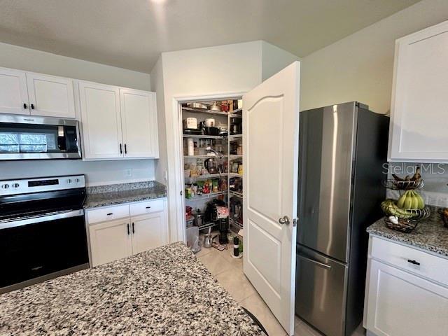 4373 Deleon St, Haines City, FL 33844 - kitchen with light tile patterned floors, stone countertops, stainless steel appliances, and white cabinetry