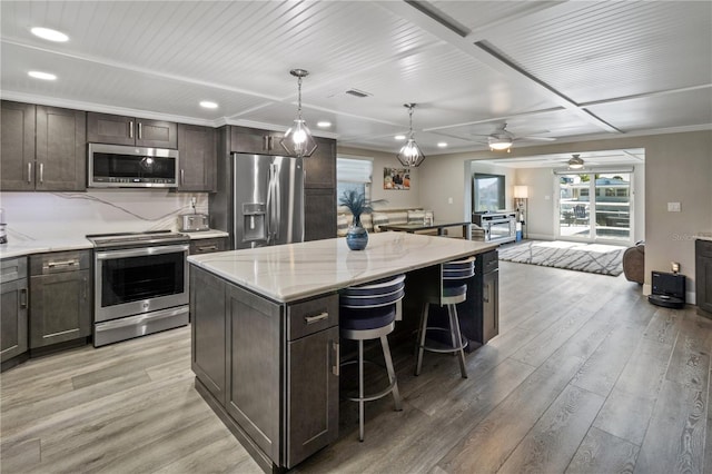 kitchen featuring ceiling fan, light wood-style flooring, a center island, and appliances with stainless steel finishes