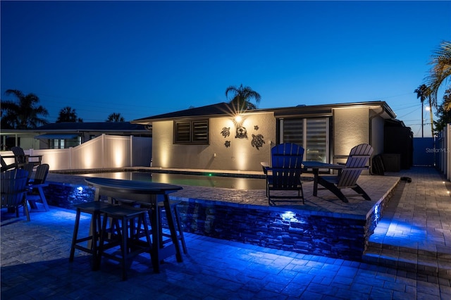 back of house at twilight with a swimming pool, stucco siding, fence, and a patio