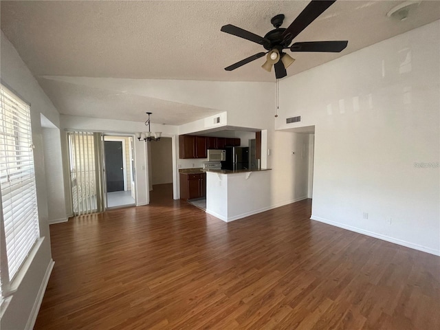 unfurnished living room featuring plenty of natural light, ceiling fan with notable chandelier, dark wood-type flooring, and visible vents