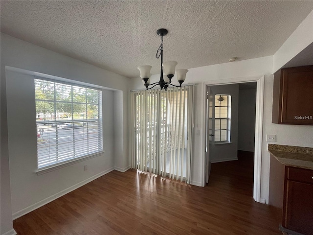 unfurnished dining area with a textured ceiling, baseboards, dark wood-style floors, and a notable chandelier