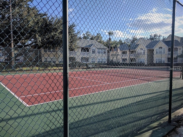 view of tennis court featuring a residential view and fence