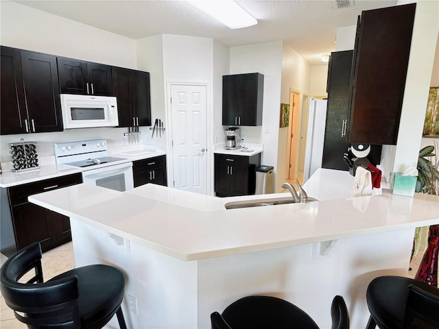kitchen with white appliances, a peninsula, a kitchen breakfast bar, and a sink
