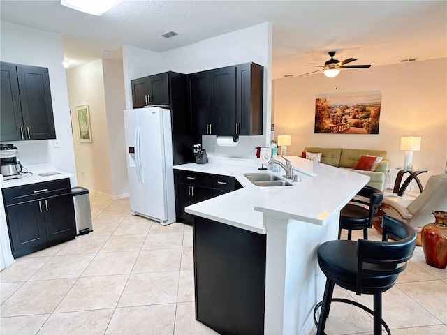 kitchen featuring a sink, a peninsula, open floor plan, white fridge with ice dispenser, and a breakfast bar