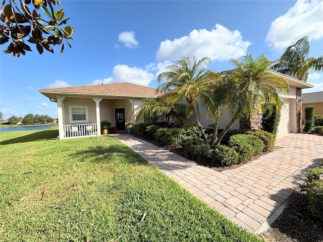 view of front facade featuring a front lawn, a garage, stucco siding, a water view, and covered porch