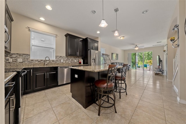 kitchen featuring appliances with stainless steel finishes, a kitchen island, backsplash, and ceiling fan