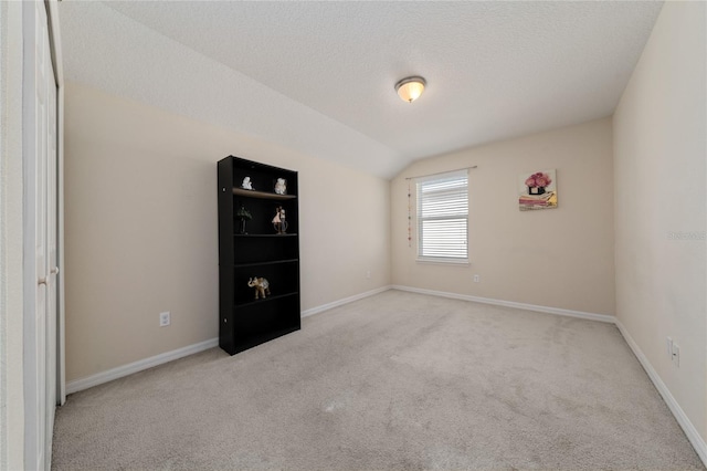carpeted spare room featuring baseboards, a textured ceiling, and lofted ceiling