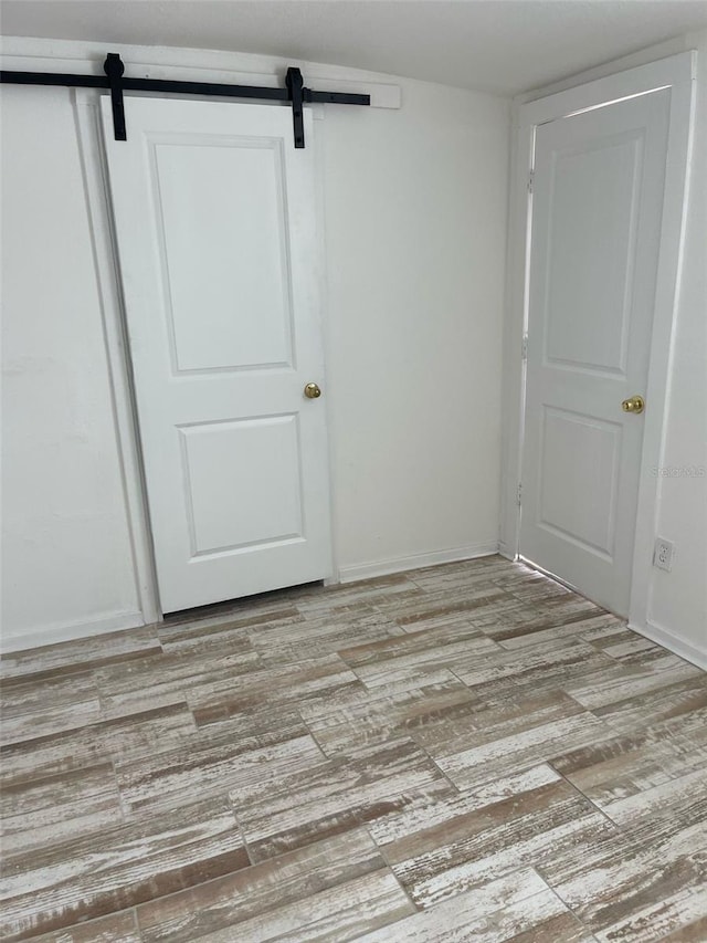unfurnished bedroom featuring a barn door, light wood-type flooring, baseboards, and a closet