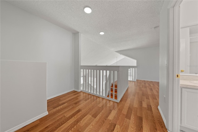 bonus room featuring light wood-style floors, baseboards, a textured ceiling, and lofted ceiling