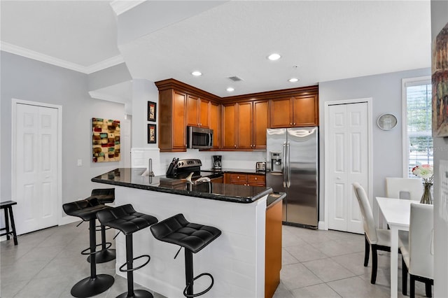 1501 Northern Harrier Way Unit 101, Kissimmee, FL 34747 - kitchen with brown cabinetry, a peninsula, light tile patterned flooring, a breakfast bar, and appliances with stainless steel finishes