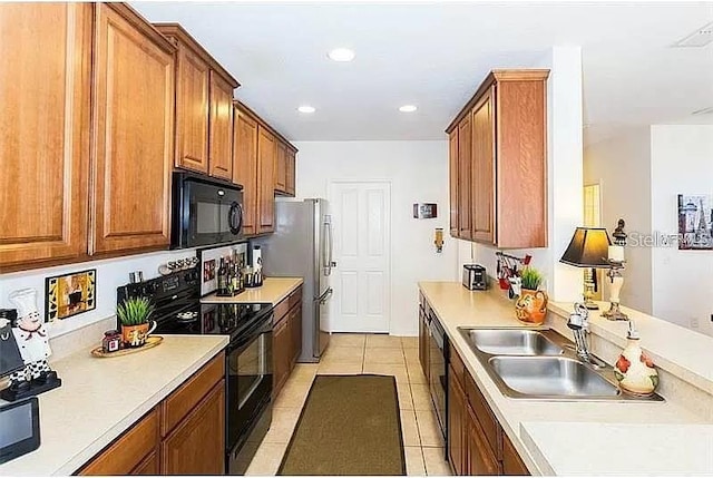 kitchen featuring light countertops, light tile patterned flooring, brown cabinetry, and black appliances