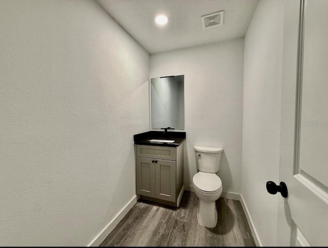 bathroom featuring visible vents, wood finished floors, baseboards, vanity, and toilet