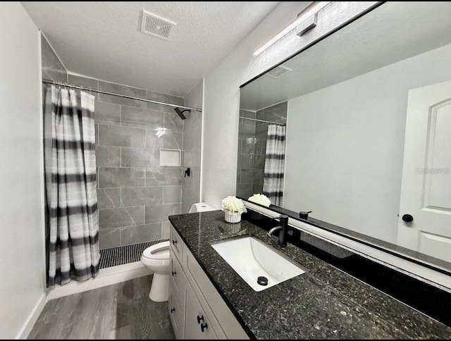 full bath with visible vents, a tile shower, wood finished floors, vanity, and toilet