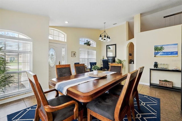 tiled dining space with arched walkways, baseboards, high vaulted ceiling, and a notable chandelier