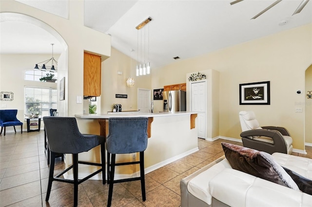 kitchen featuring light tile patterned flooring, stainless steel fridge with ice dispenser, brown cabinetry, a peninsula, and a kitchen bar