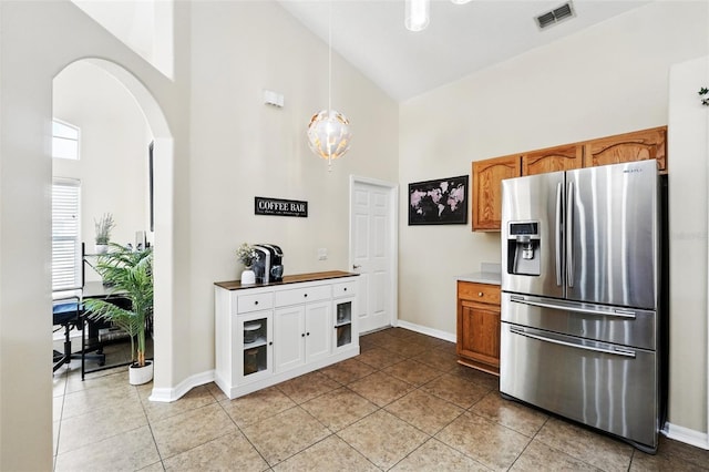 kitchen featuring arched walkways, high vaulted ceiling, light tile patterned floors, stainless steel refrigerator with ice dispenser, and visible vents