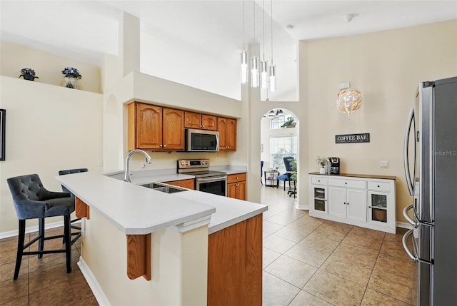 kitchen with a high ceiling, brown cabinets, a sink, light tile patterned floors, and stainless steel appliances