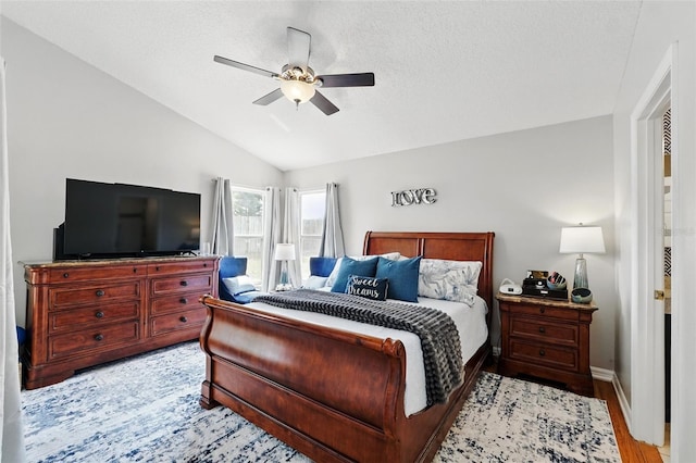 bedroom with ceiling fan, light wood finished floors, a textured ceiling, baseboards, and lofted ceiling