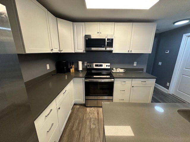 8702 El Portal Dr, Tampa, FL 33604 - kitchen featuring appliances with stainless steel finishes, dark wood finished floors, white cabinets, and dark countertops