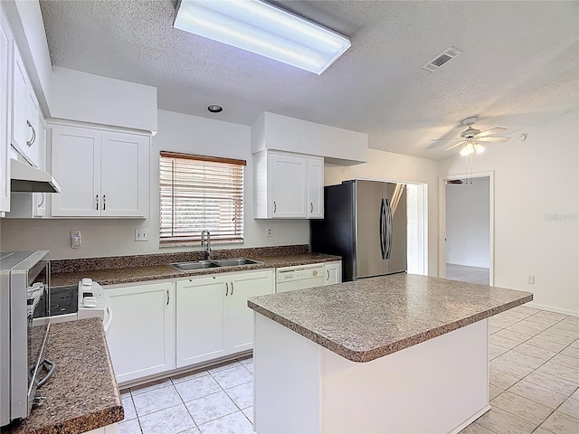 kitchen with a ceiling fan, a textured ceiling, a sink, freestanding refrigerator, and under cabinet range hood