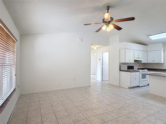 kitchen with a textured ceiling, stainless steel microwave, white range with gas stovetop, light tile patterned floors, and vaulted ceiling