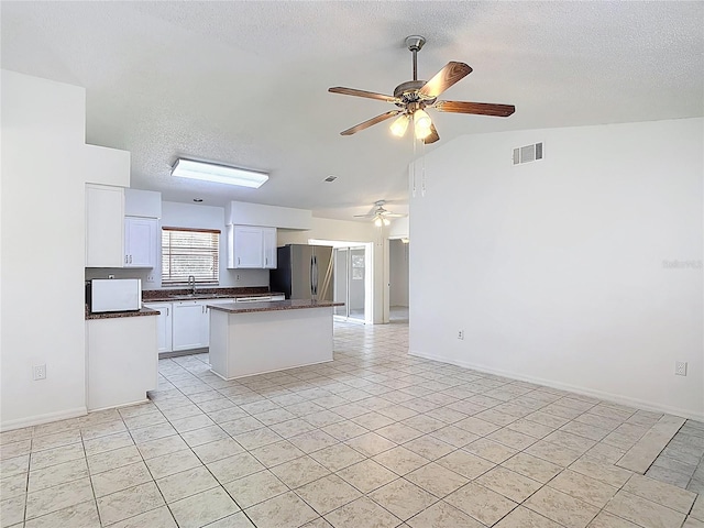 kitchen featuring dark countertops, a sink, a textured ceiling, freestanding refrigerator, and open floor plan