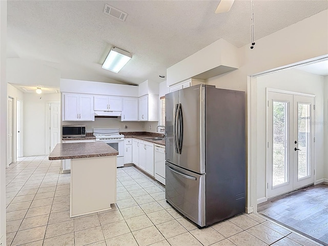 kitchen with light tile patterned flooring, dark countertops, appliances with stainless steel finishes, lofted ceiling, and under cabinet range hood
