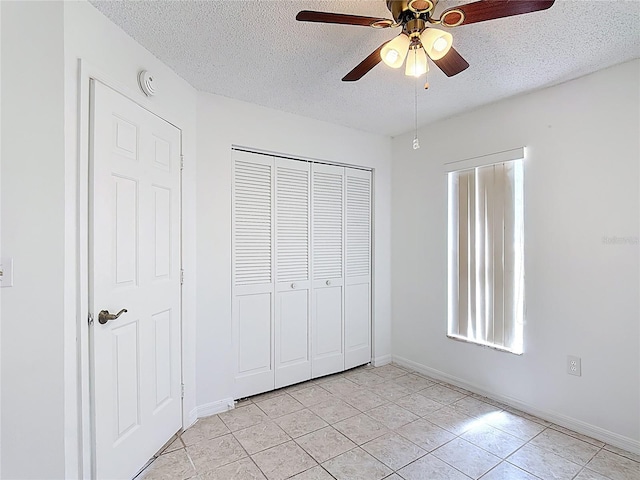unfurnished bedroom with ceiling fan, a textured ceiling, light tile patterned floors, baseboards, and a closet