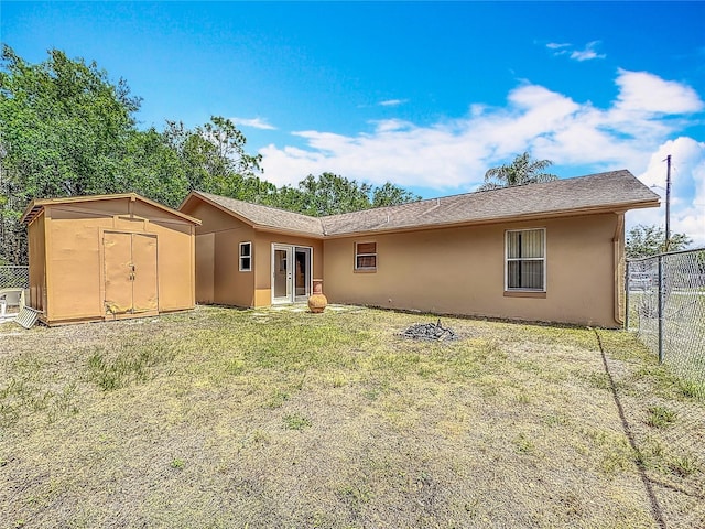 rear view of property with fence, an outdoor structure, a shed, a yard, and stucco siding
