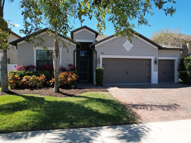 ranch-style home featuring decorative driveway, a garage, a front lawn, and stucco siding