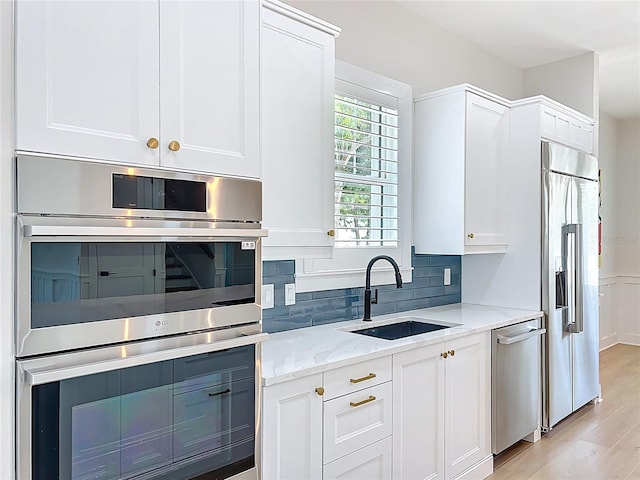 kitchen with light stone countertops, white cabinetry, tasteful backsplash, a sink, and appliances with stainless steel finishes