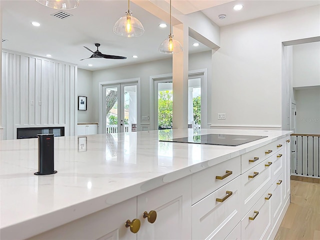 kitchen with light stone countertops, black electric cooktop, a ceiling fan, white cabinetry, and visible vents