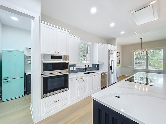 kitchen with white cabinets, light stone counters, a sink, light wood-style floors, and stainless steel appliances