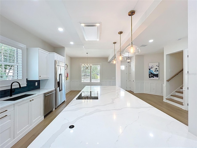 kitchen with wainscoting, a decorative wall, white cabinets, a sink, and stainless steel appliances
