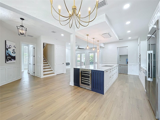 kitchen with an inviting chandelier, light wood finished floors, a decorative wall, light countertops, and beverage cooler