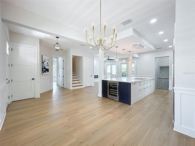 kitchen with visible vents, beverage cooler, an island with sink, light countertops, and light wood finished floors