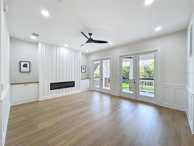 unfurnished living room with a healthy amount of sunlight, a decorative wall, a ceiling fan, and french doors