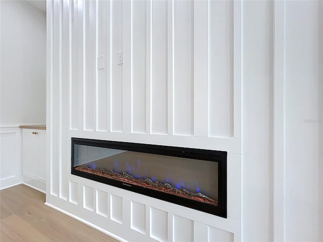 interior details with a glass covered fireplace, a wainscoted wall, a decorative wall, and wood finished floors