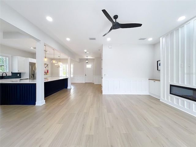 unfurnished living room with wainscoting, ceiling fan, plenty of natural light, and a decorative wall
