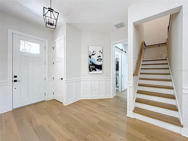 foyer featuring visible vents, light wood-style floors, stairway, a textured ceiling, and a wainscoted wall