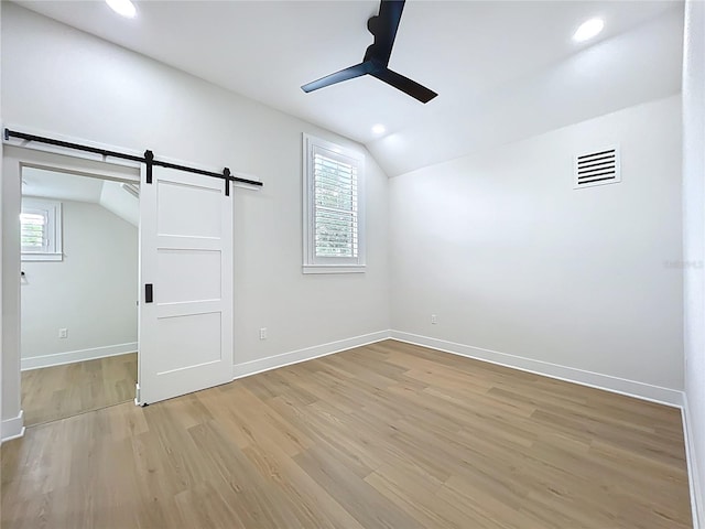 additional living space with ceiling fan, a barn door, baseboards, lofted ceiling, and light wood-type flooring