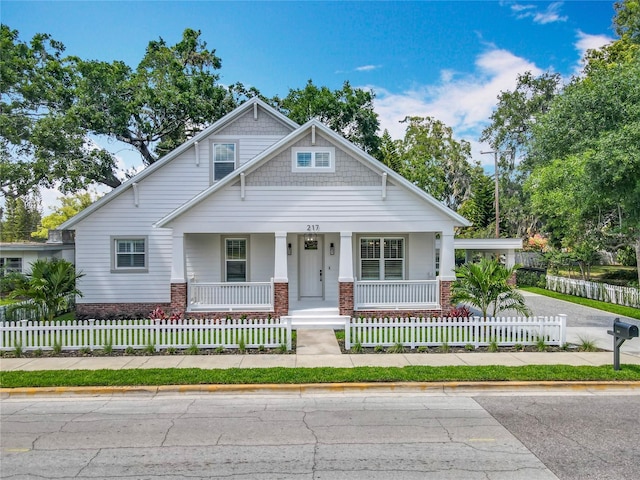 view of front facade featuring covered porch, brick siding, and a fenced front yard