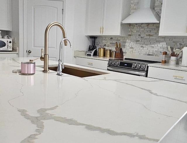 kitchen featuring decorative backsplash, stainless steel range with electric stovetop, white microwave, custom exhaust hood, and white cabinetry