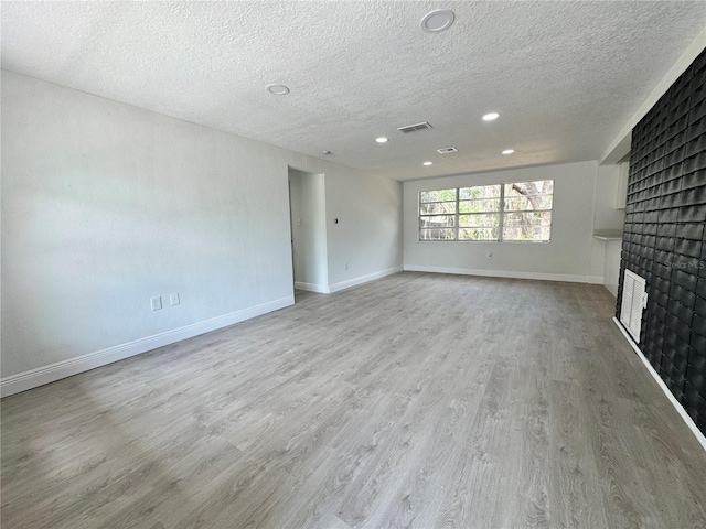 unfurnished living room with a textured ceiling, visible vents, a brick fireplace, wood finished floors, and recessed lighting