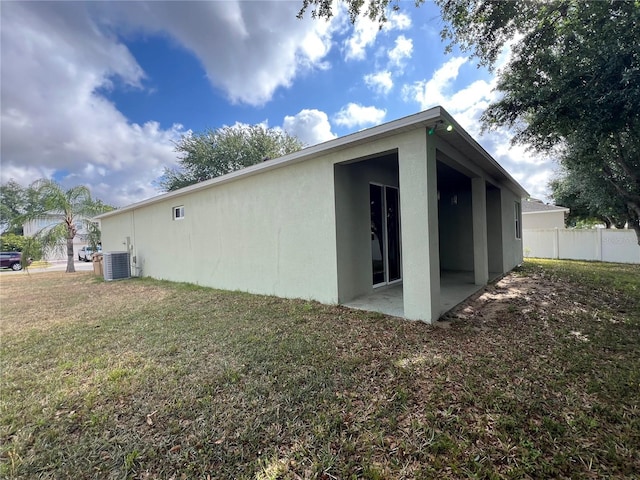 rear view of property featuring fence, stucco siding, cooling unit, a patio area, and a lawn