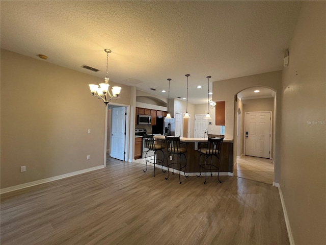 kitchen featuring a kitchen breakfast bar, visible vents, arched walkways, light wood finished floors, and stainless steel appliances